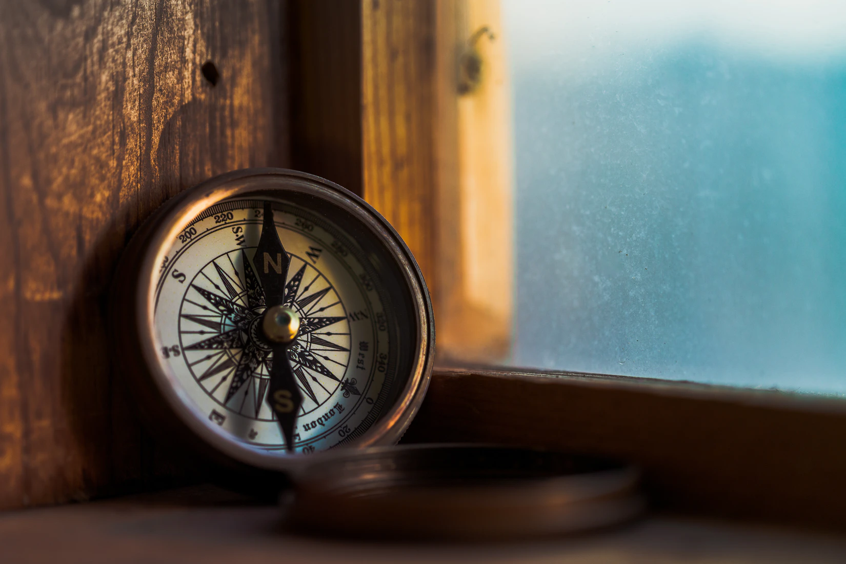 A compass sits on a windowsill overlooking the sea.